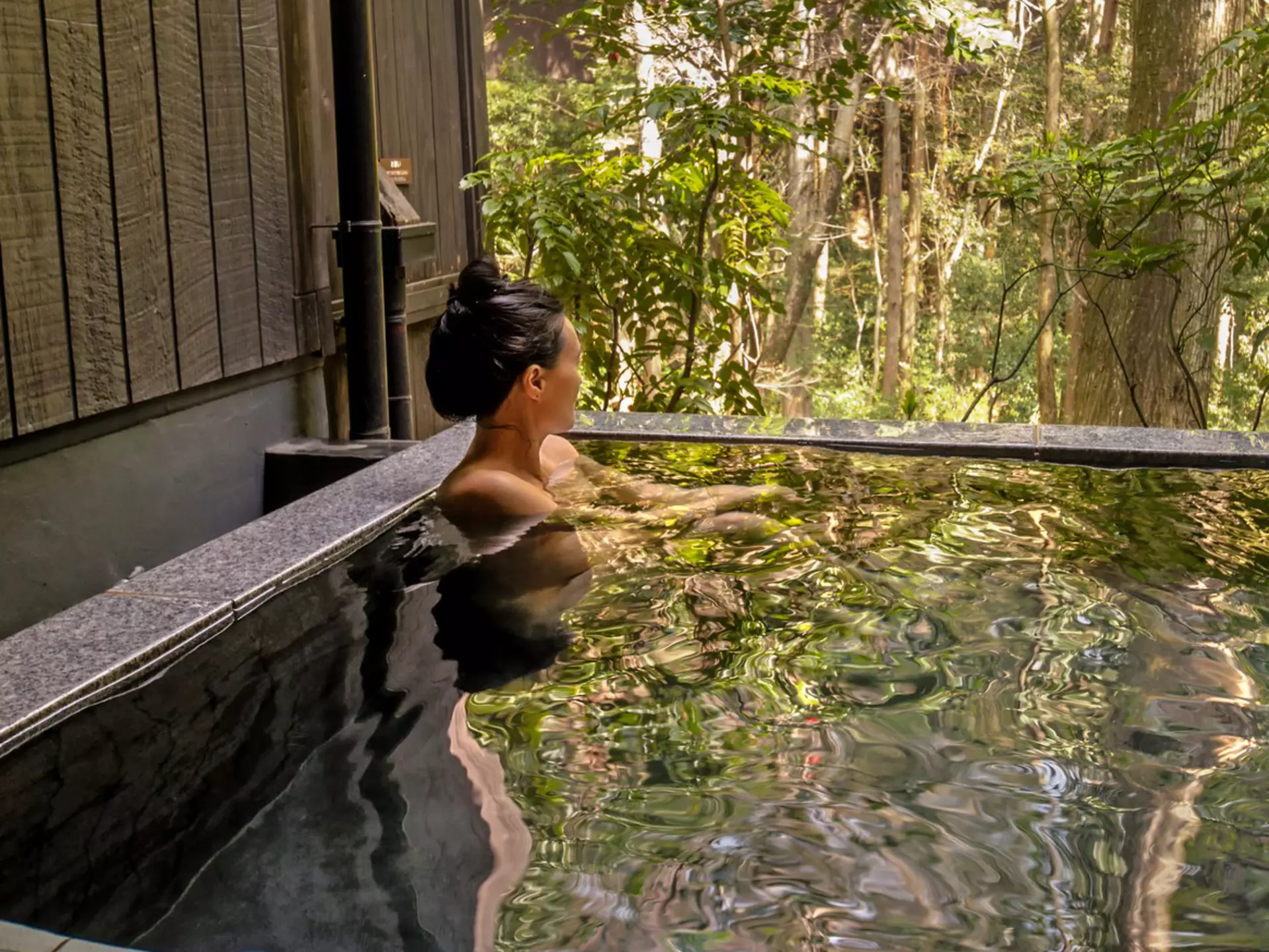 A person sitting in a clear outdoor pool lined with rocks.
