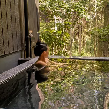 A person sitting in a clear outdoor pool lined with rocks.