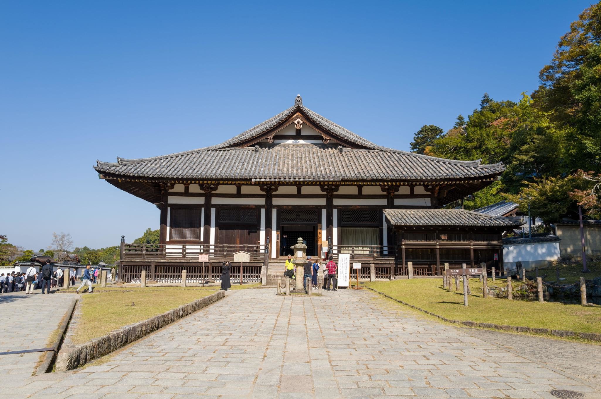 **RIGHTS MANAGED** Uploaded for use on the LP APP

Nara, Japan - November 3, 2023: The image shows the front view of Todai-ji Hokkedo main hall with traditional Japanese architecture, tiled roof, and groups of visitors standing on the stone path under a clear blue sky.