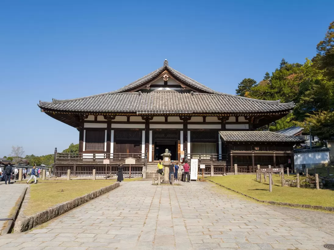 **RIGHTS MANAGED** Uploaded for use on the LP APP

Nara, Japan - November 3, 2023: The image shows the front view of Todai-ji Hokkedo main hall with traditional Japanese architecture, tiled roof, and groups of visitors standing on the stone path under a clear blue sky.
