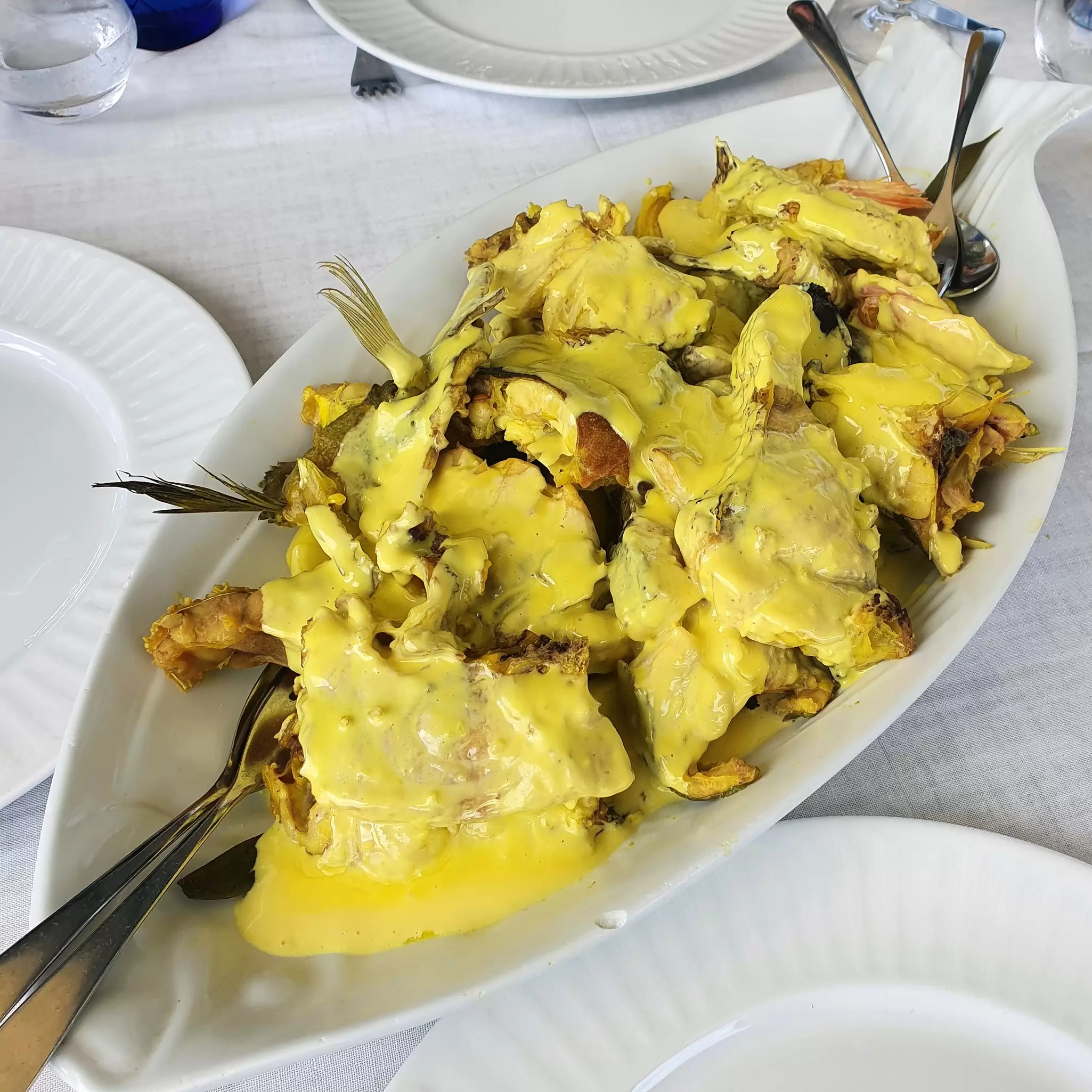 A large platter of mixed fish covered in yellow sauce on a table.