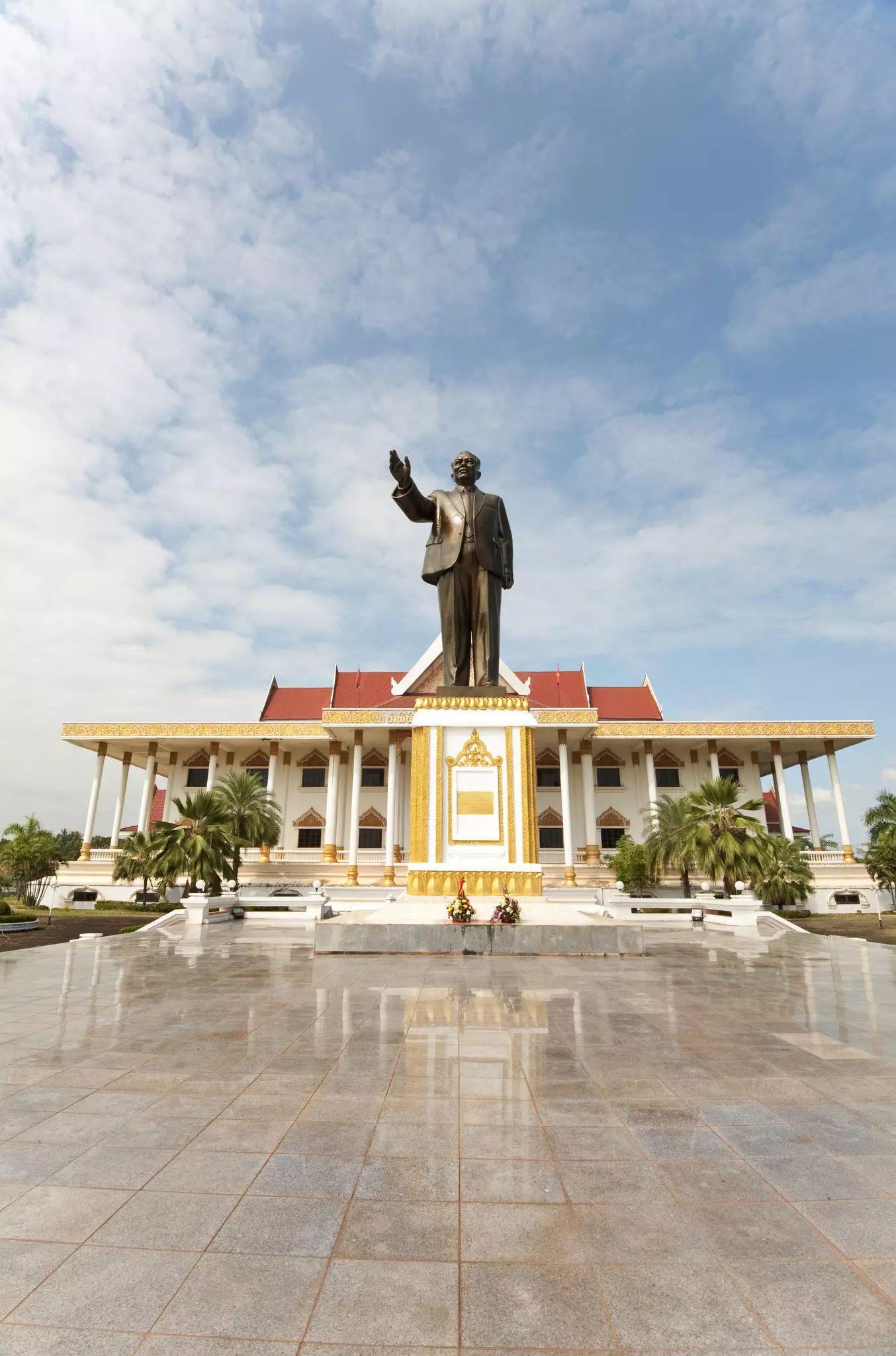 A large statue of a man, waving his right hand, stands outside a museum