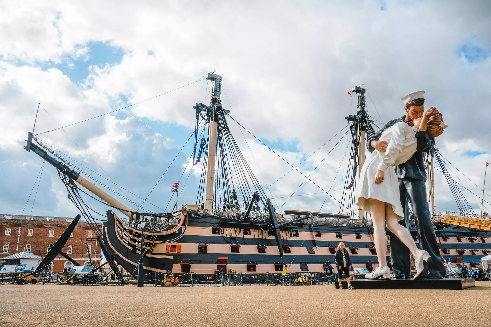 A large wooden ship in a dry dock. A sculpture of a sailor and woman kissing stand nearby.