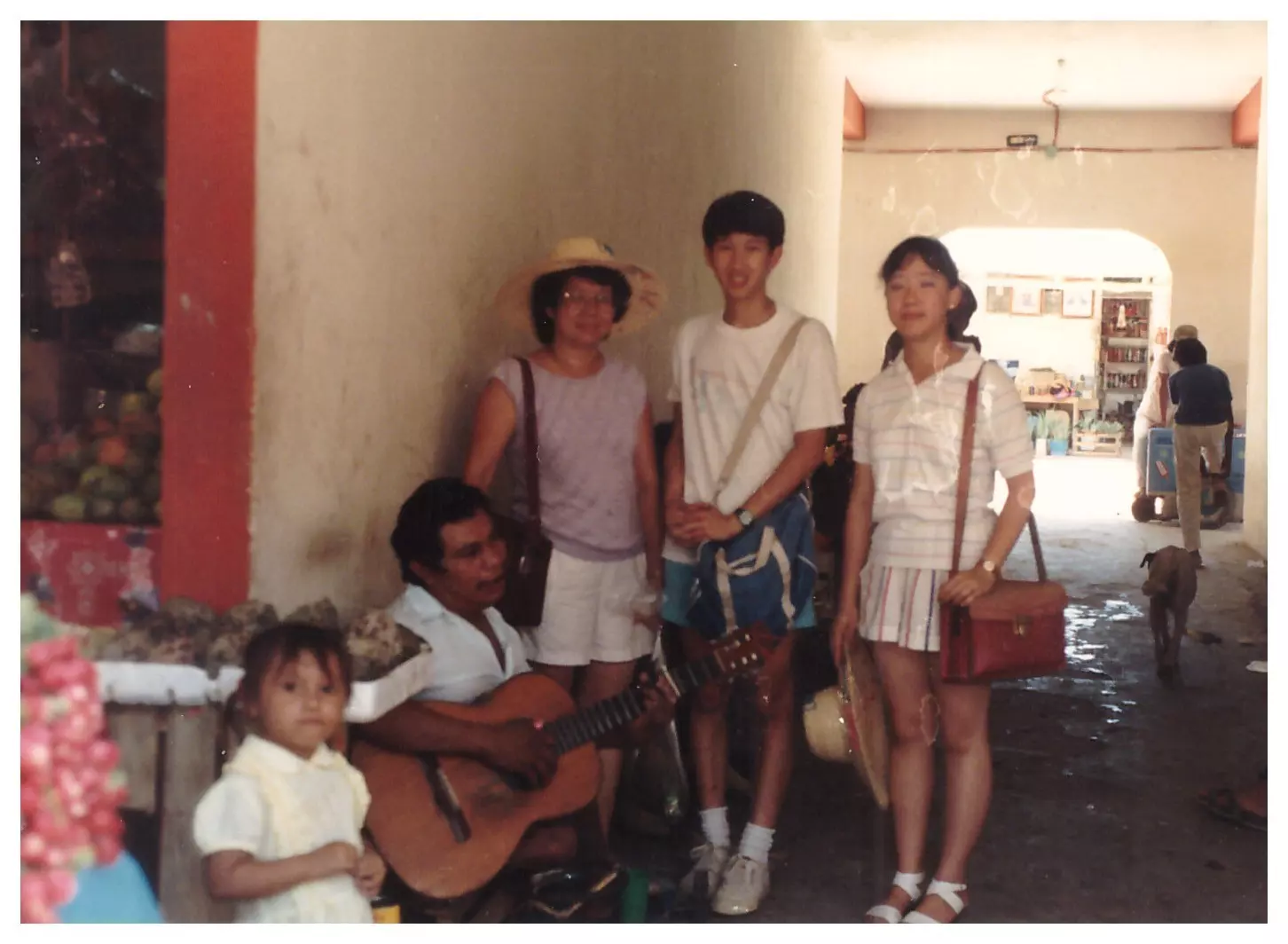 An older photo of a family on vacation next to a man playing guitar in a covered alleyway.