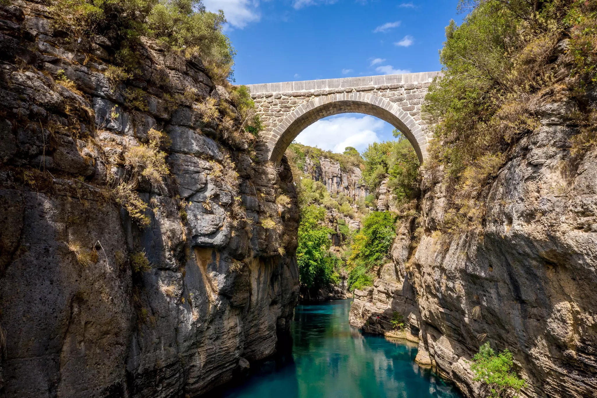 An ancient arched stone bridge over a river in a scenic gorge in Turkey.