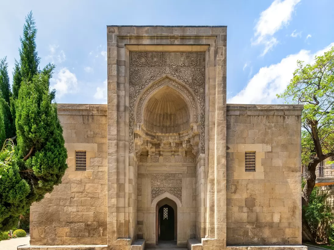 Exterior of the mausoleum and surrounding trees in the Palace of the Shirvanshahs complex. Intricate stonework and a serene setting, reflecting Azerbaijan's rich history. Baku, Azerbaijan.