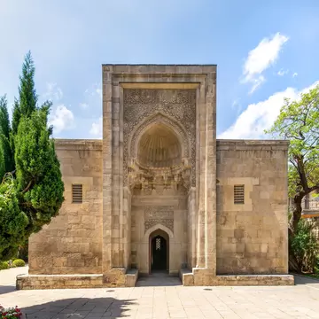 Exterior of the mausoleum and surrounding trees in the Palace of the Shirvanshahs complex. Intricate stonework and a serene setting, reflecting Azerbaijan's rich history. Baku, Azerbaijan.
