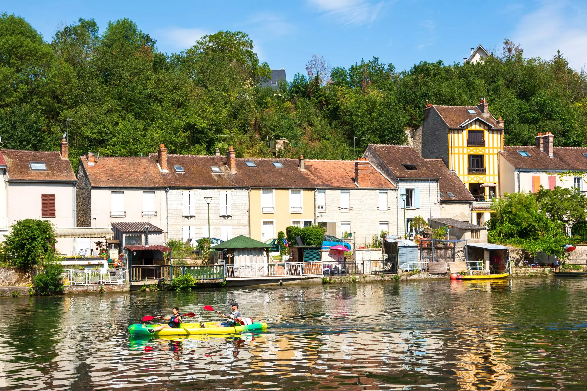 A couple paddling a kayak on a river with picturesque houses in the background.