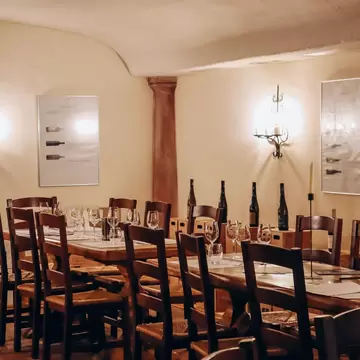 Candlelit vaulted cellar room with a long wooden table and chairs, wine bottles and wall sconces at the Hofkellerei