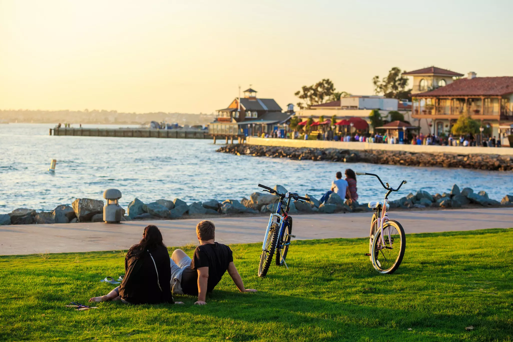 Two people sit in grass by their bikes as they watch the sunset by an ocean