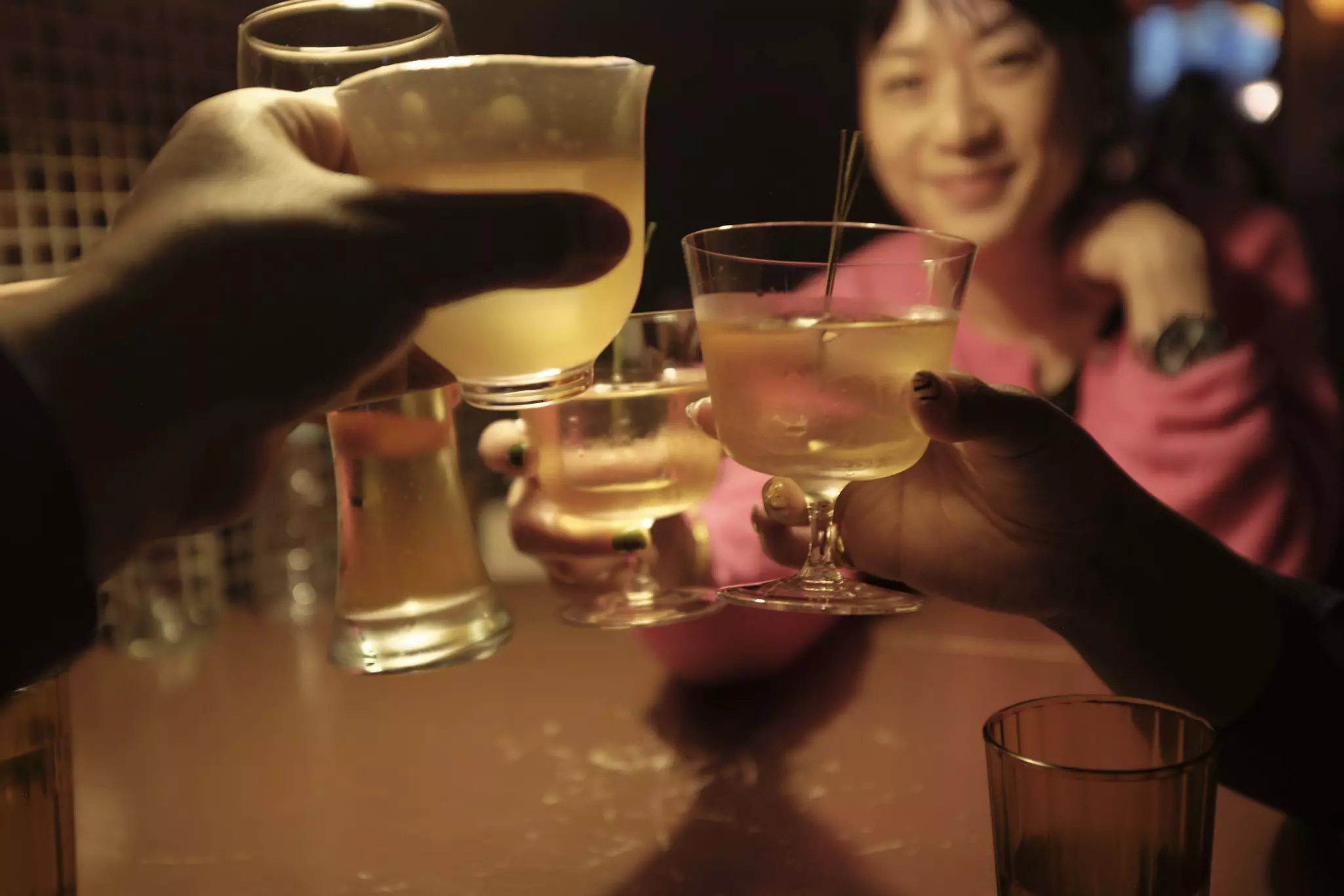 A close of up of people raising cocktails to clink at a dimly lit bar.