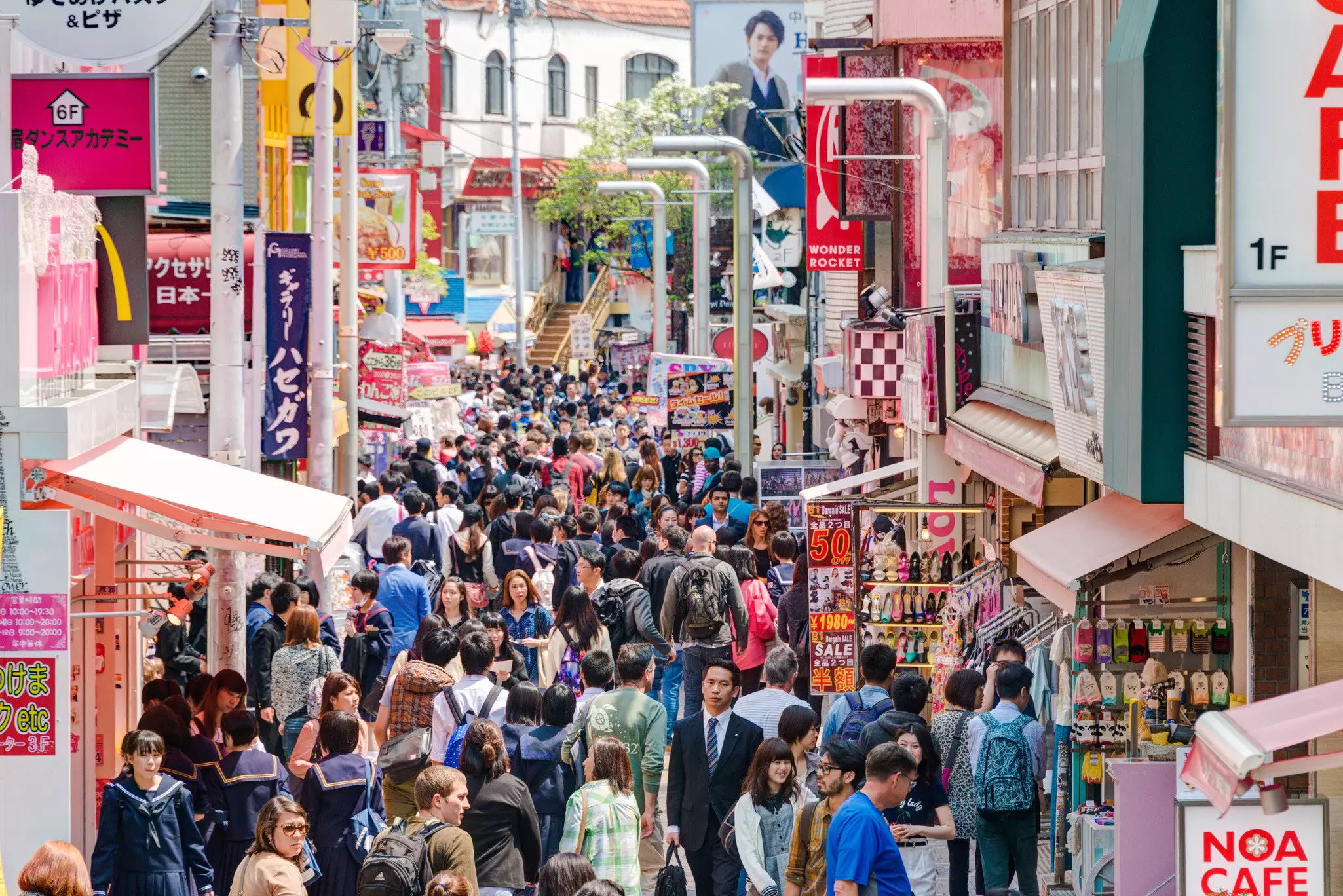 Pedestrians on a crowded street filled with shops, cafes and signs.