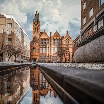 Brindley Place red brick church building reflected in water. West Midlands landmark buildings redevelopment in historic city centre reflection in stream. Birds and clouds in sky.