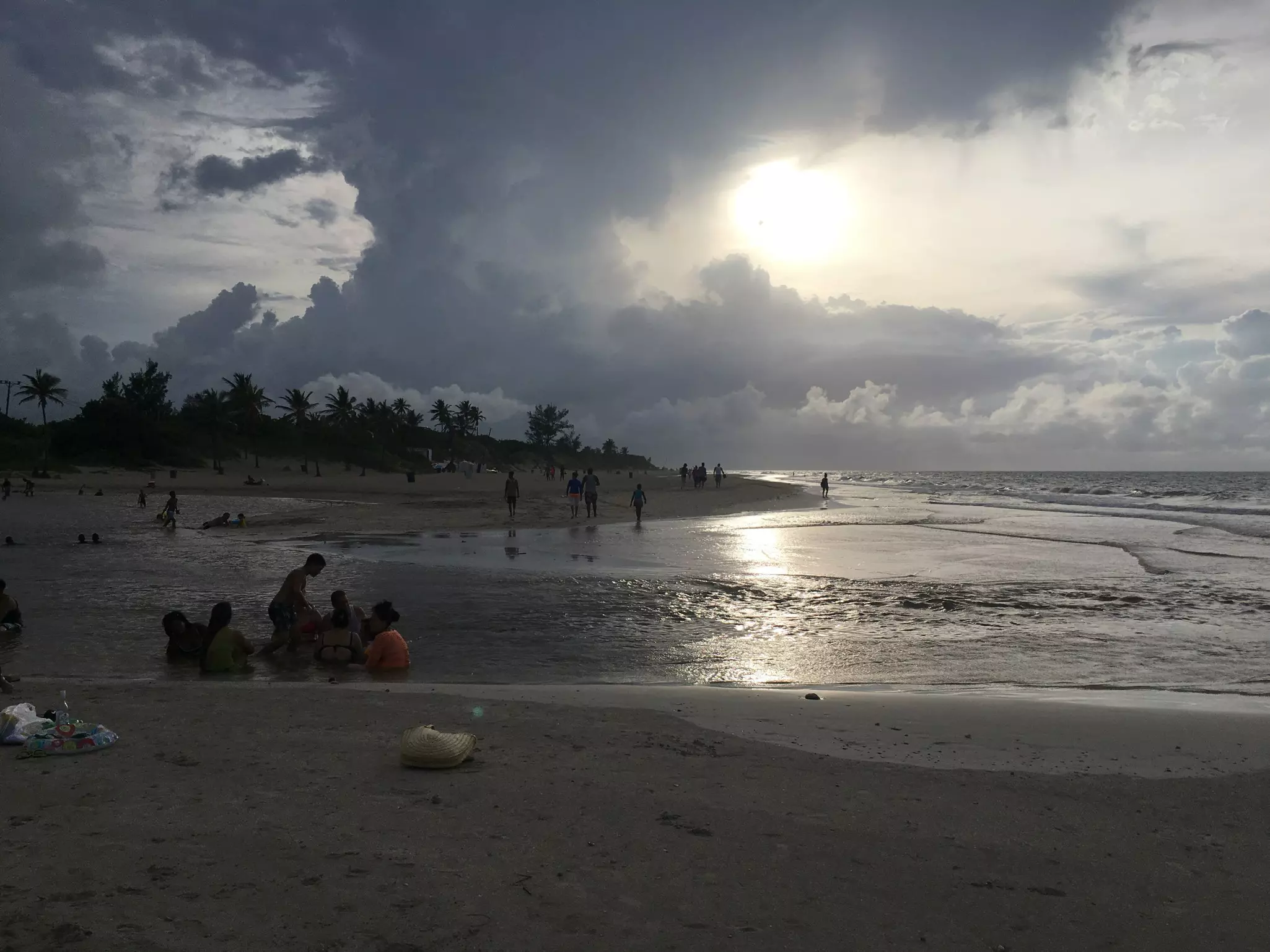 People walking and sitting by the shoreline of a beach on a cloudy day