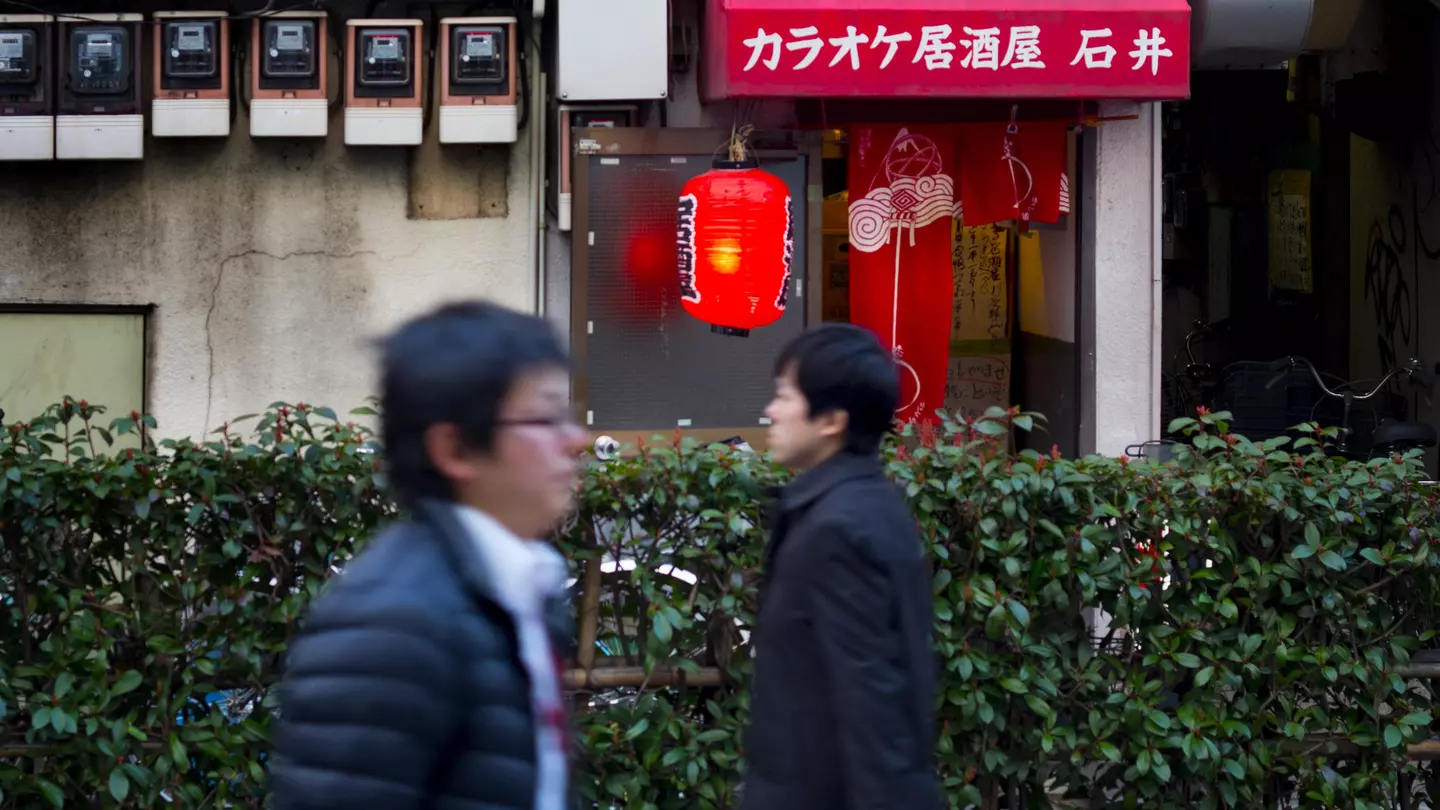Two men walking in opposite directions past a karaoke bar near the Kita-Senju train station in Northern Tokyo