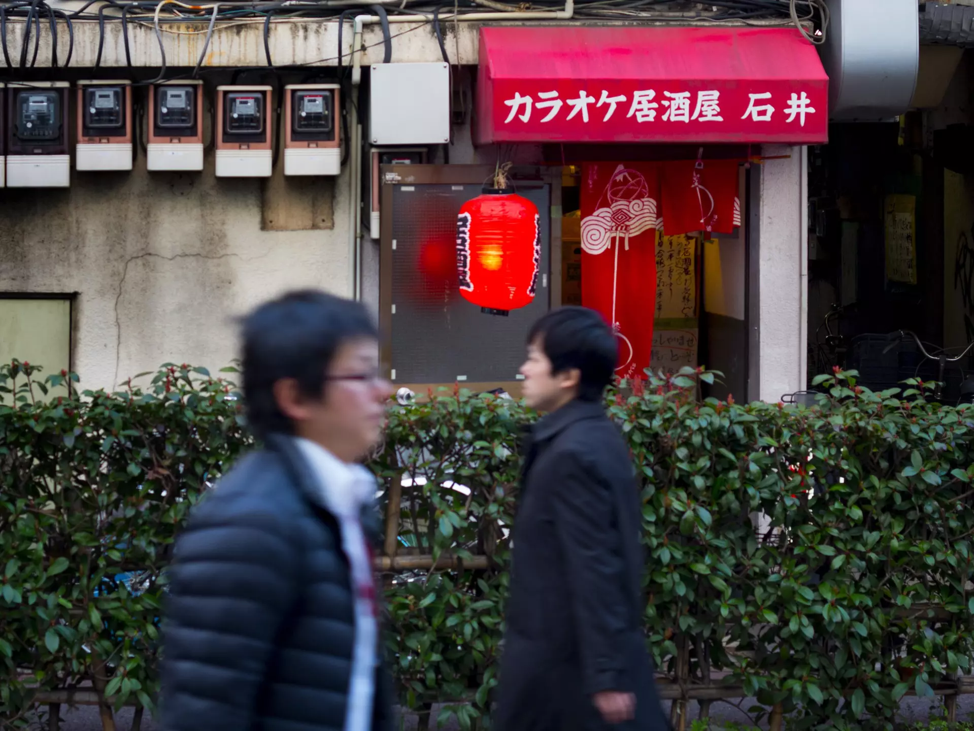 Two men walking in opposite directions past a karaoke bar near the Kita-Senju train station in Northern Tokyo