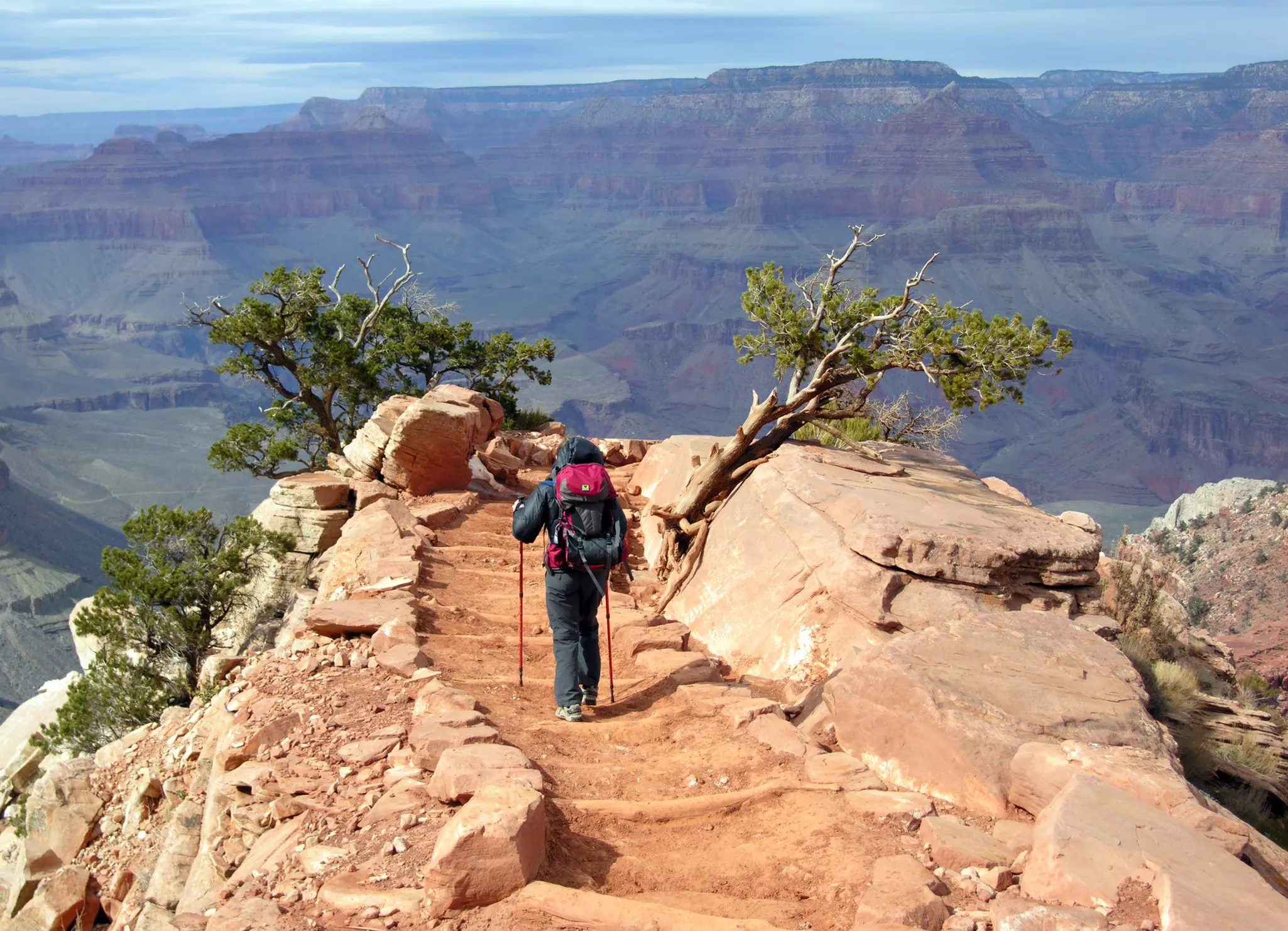 A hiker follows a narrow uneven pathway in a vast canyon.