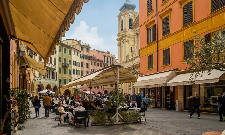 Santa Margherita Ligure piazza: people at awning-shaded café tables beside orange facades and a yellow clock tower