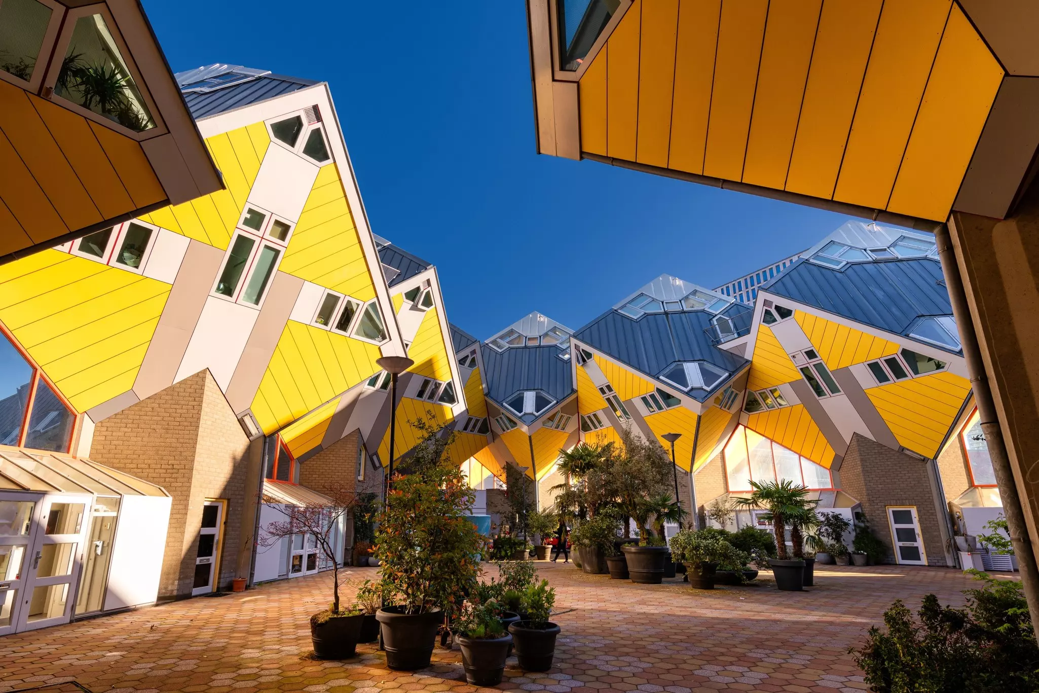 A series of cube-shaped yellow buildings that appear to sink forward into a courtyard, defying gravity