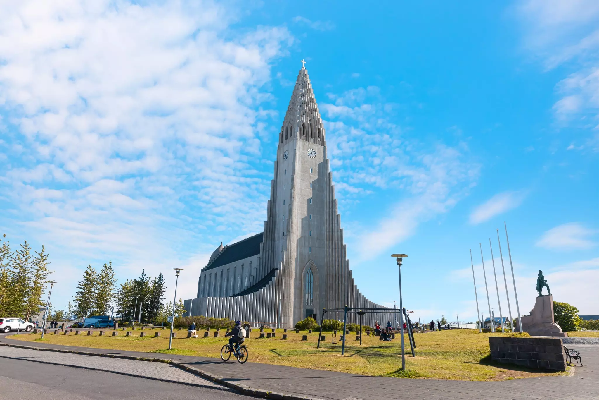 Hallgrímskirkja Lutheran parish church on a sunny day with trees, grass and a cyclist in the foreground