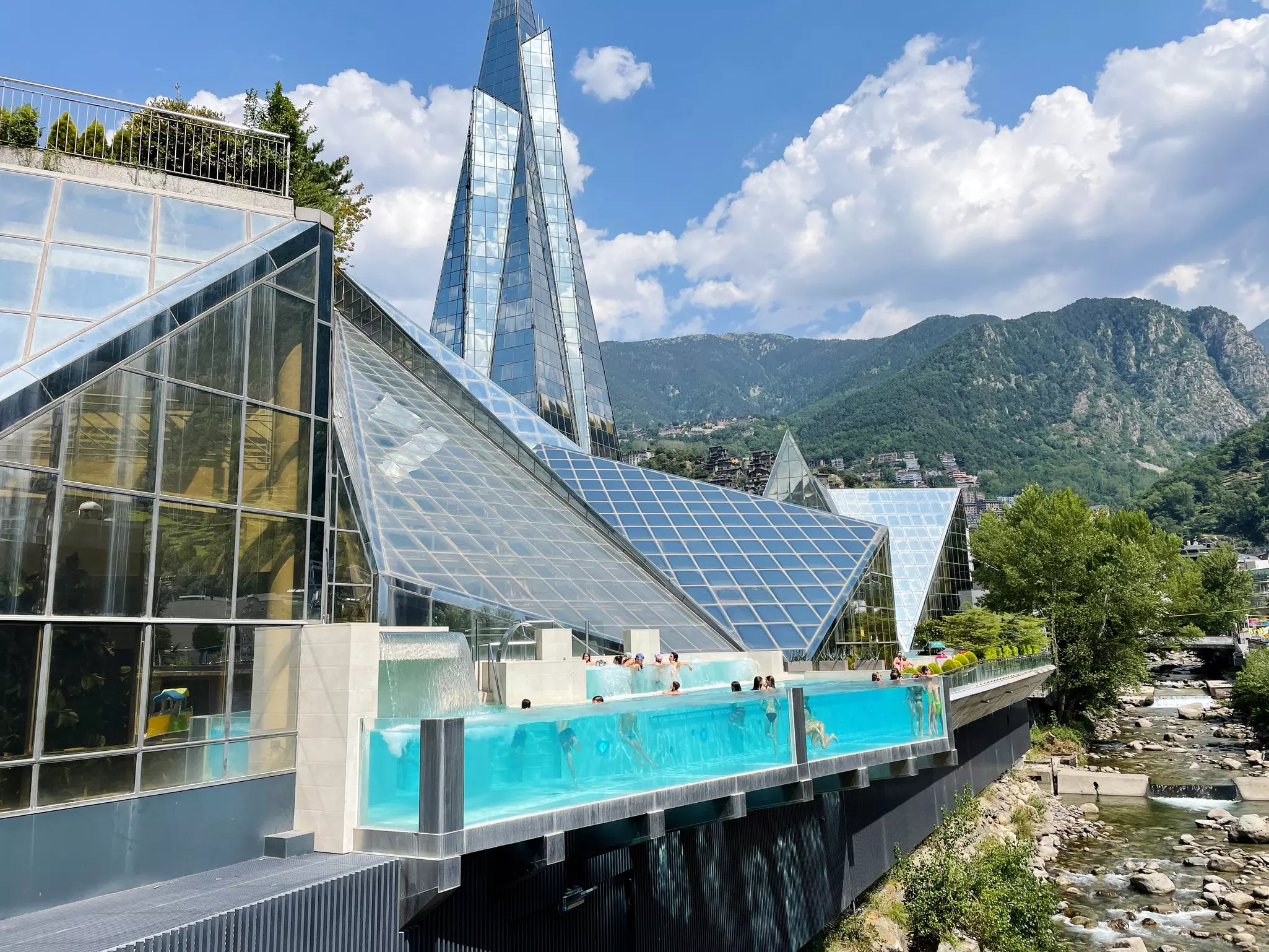 A triangular-shaped spa building with people in a small pool and mountains in background