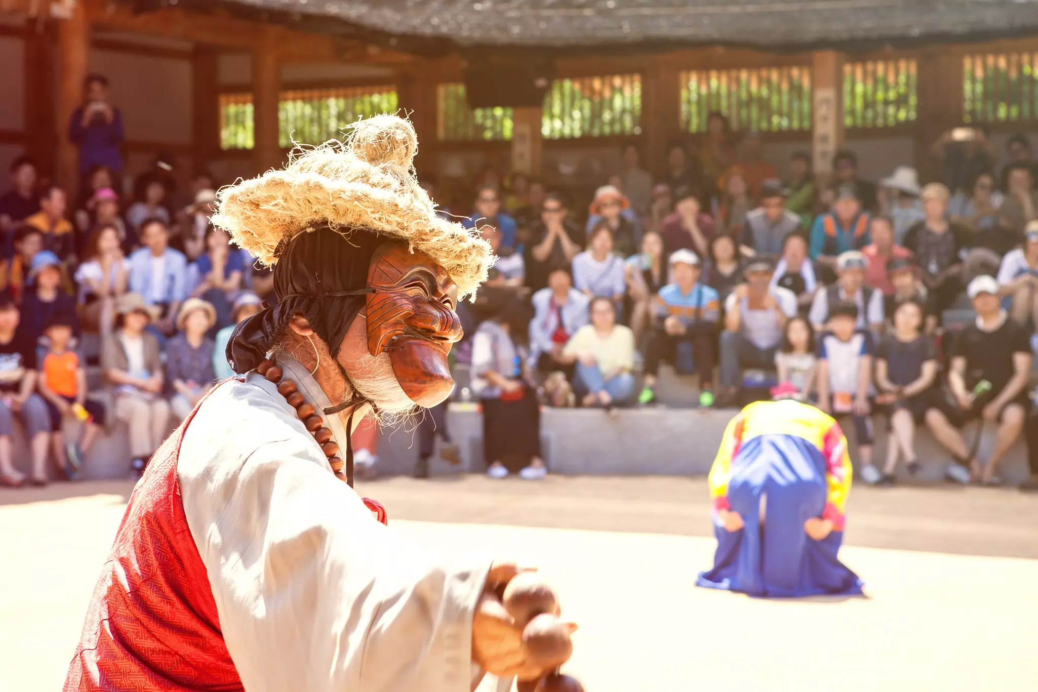 A performer in a traditional Korean mask at Andong's Hahoe Folk Village in front of spectators