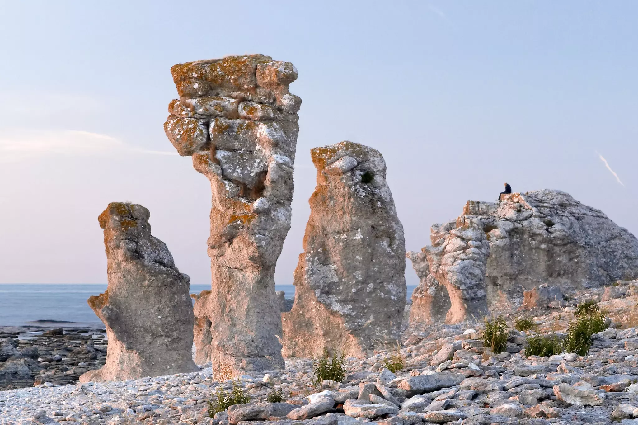 Huge freestanding stones on a rocky coastline. A person sits on one that they've climbed