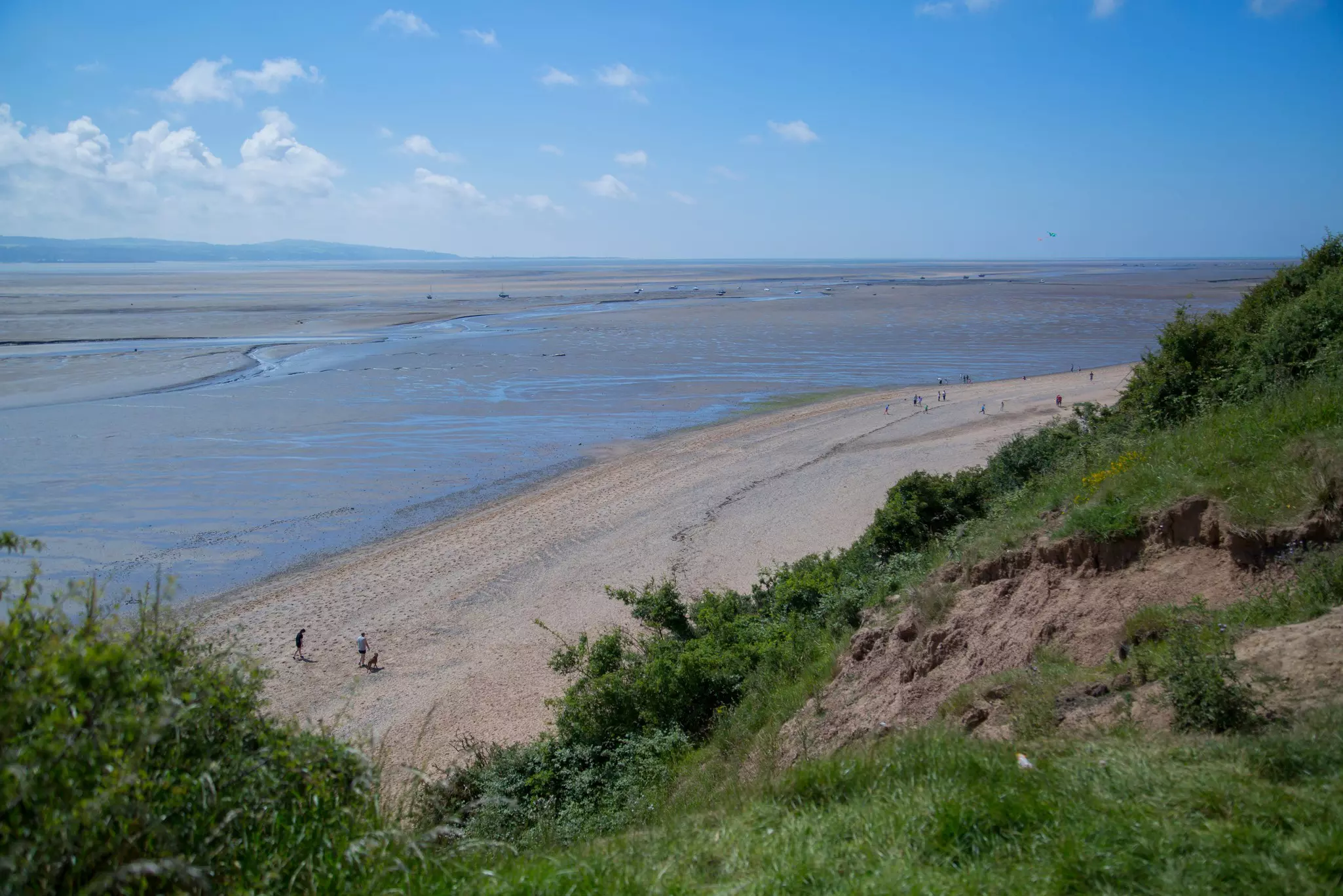 People walk on a large sandy beach backed by grass-topped cliffs