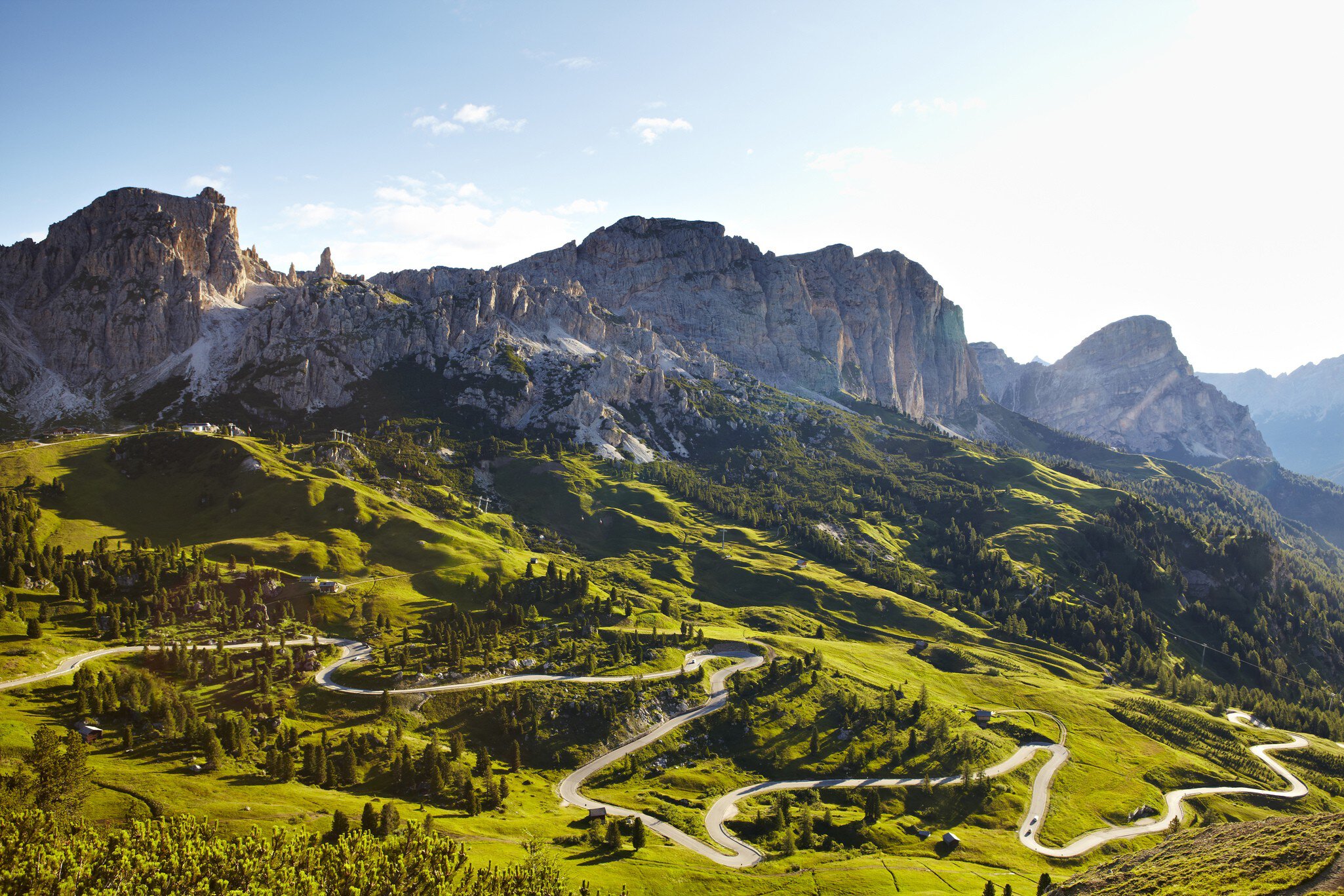 Overview of road winding through valley below Italian Alps.