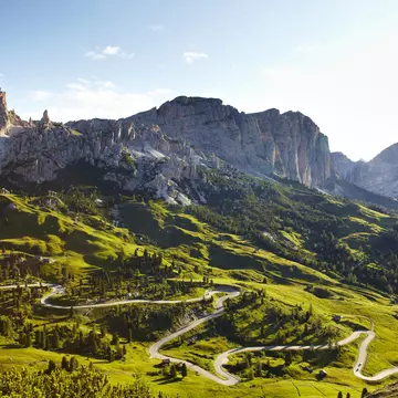 Overview of road winding through valley below Italian Alps.