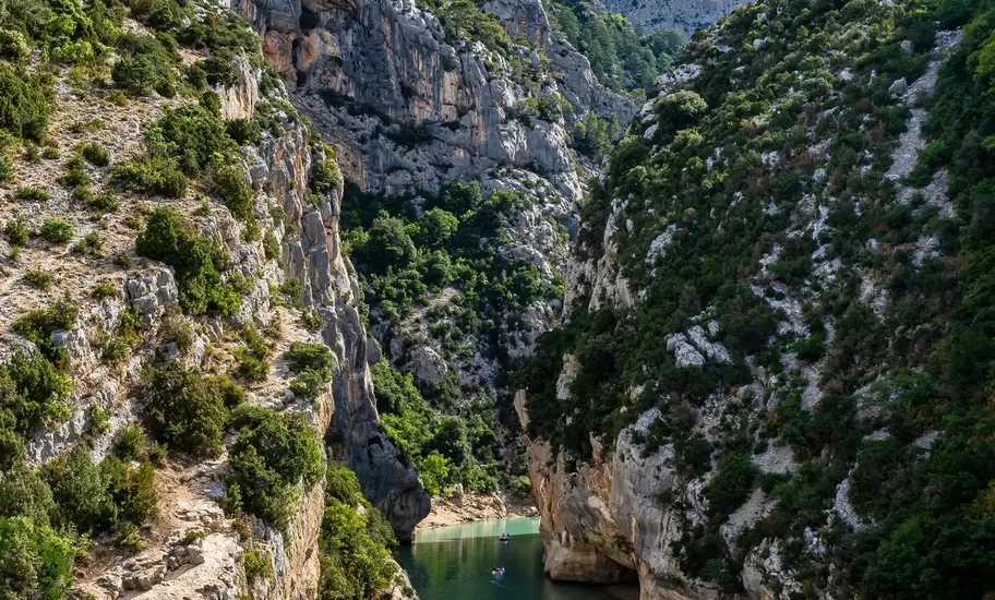 Sheer limestone cliffs and scrubby slopes of the Gorges du Verdon closing around a green river dotted with small boats