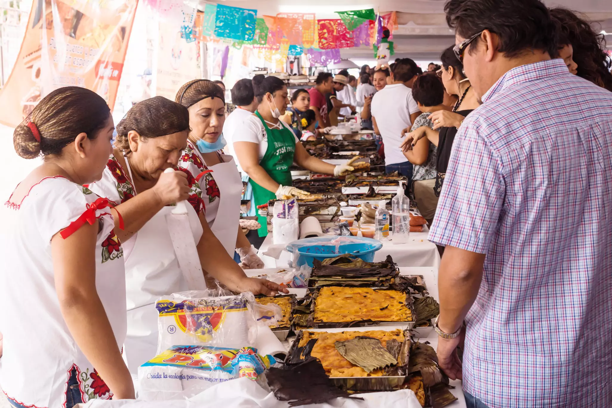 People sell traditional prepared food at a crowded covered market.