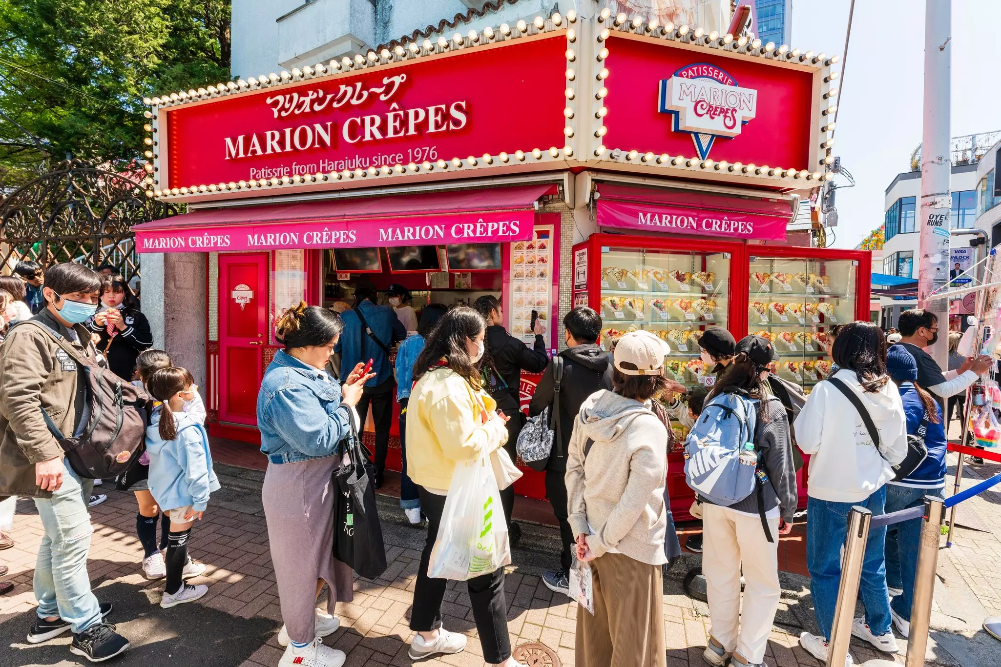 People wait in line in front of a crêpe shop on a crowded city street.