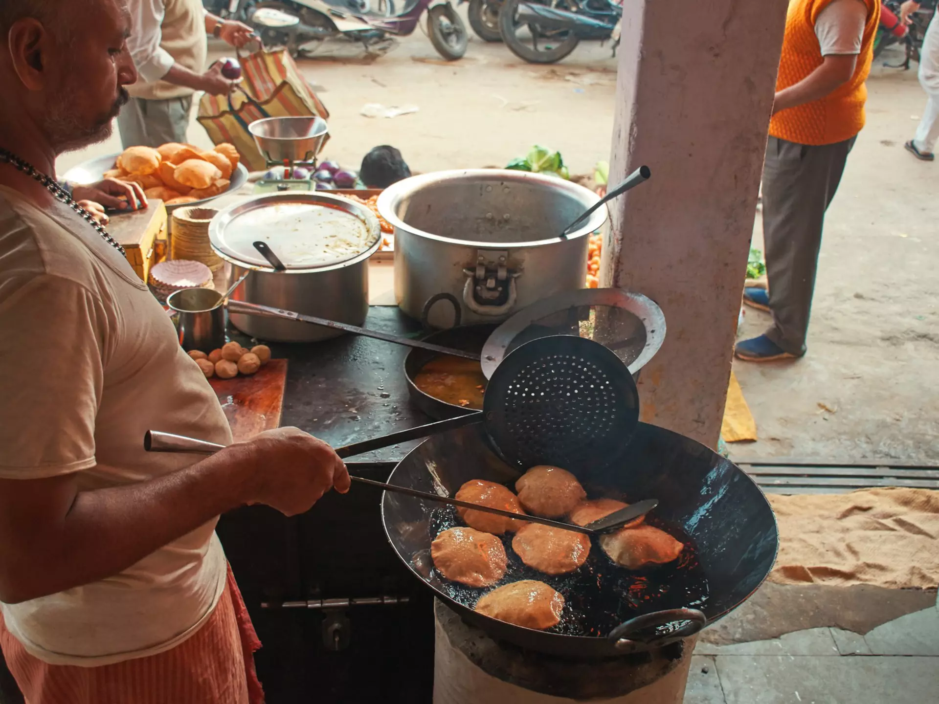 A man cooks a dish at a stall in a roadside stand in a city.