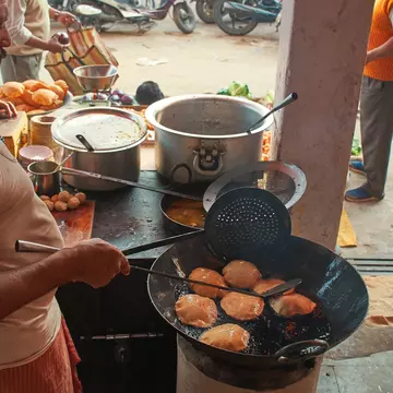 A man cooks a dish at a stall in a roadside stand in a city.