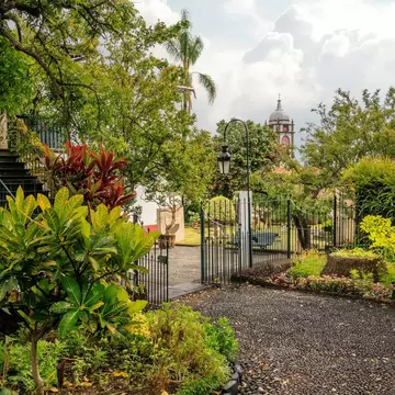 Leafy garden with red and green tropical plants, a lamp post and iron gate at Quinta das Cruzes in Funchal