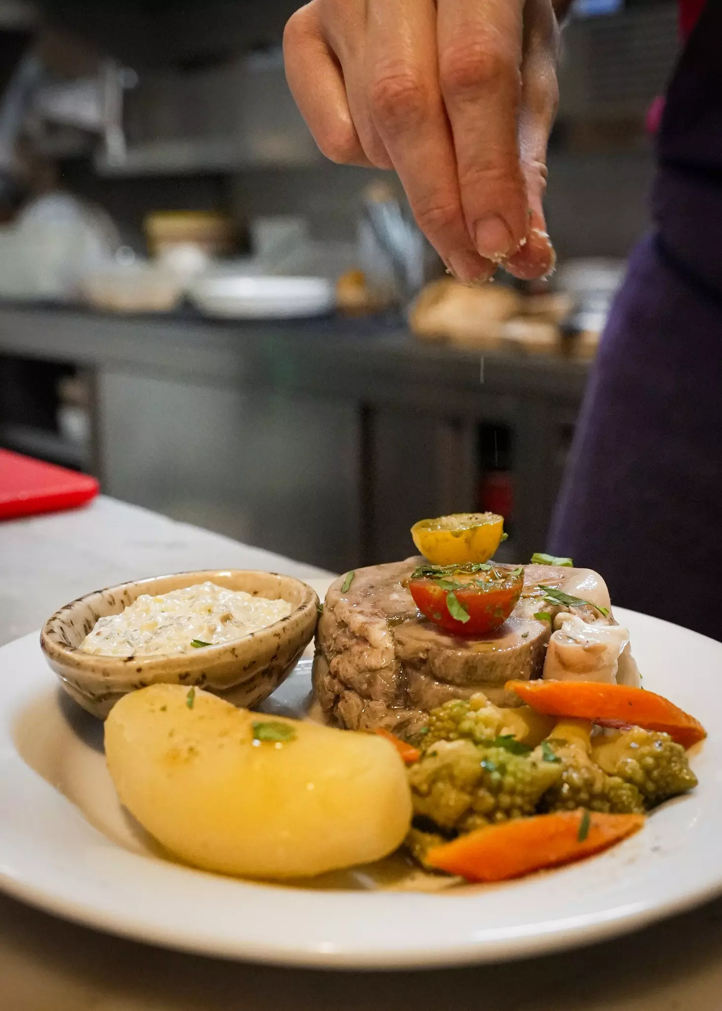A meat, potato and vegetable dish being  prepared in a restaurant kitchen