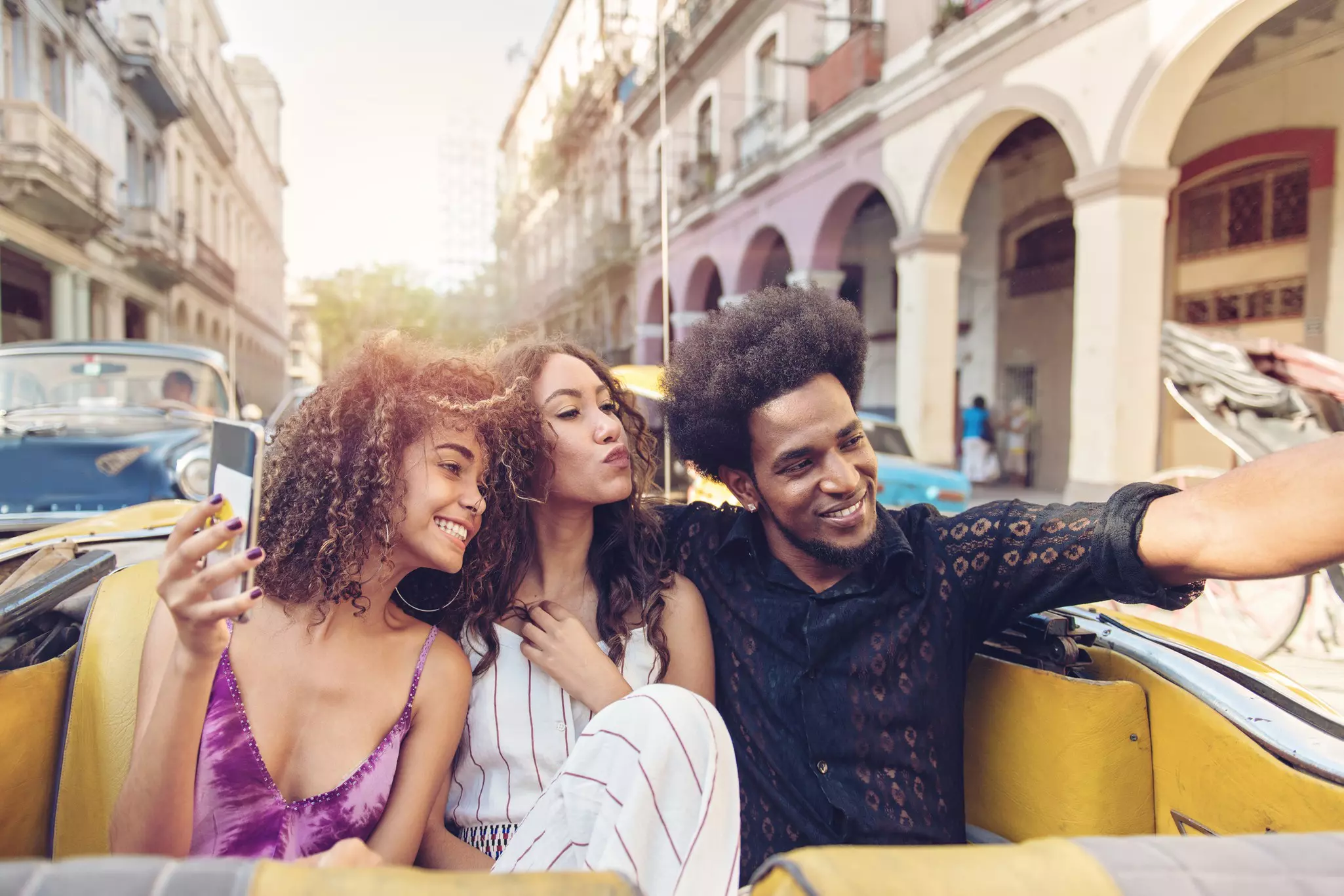 Three friends smile as they ride along in the back of a convertible car