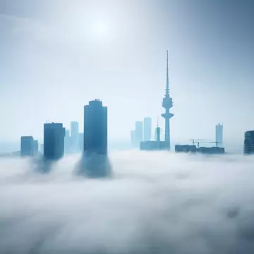Kuwait City skyline with Liberation Tower's spire and office towers poking out of a thick layer of fog under a hazy sun