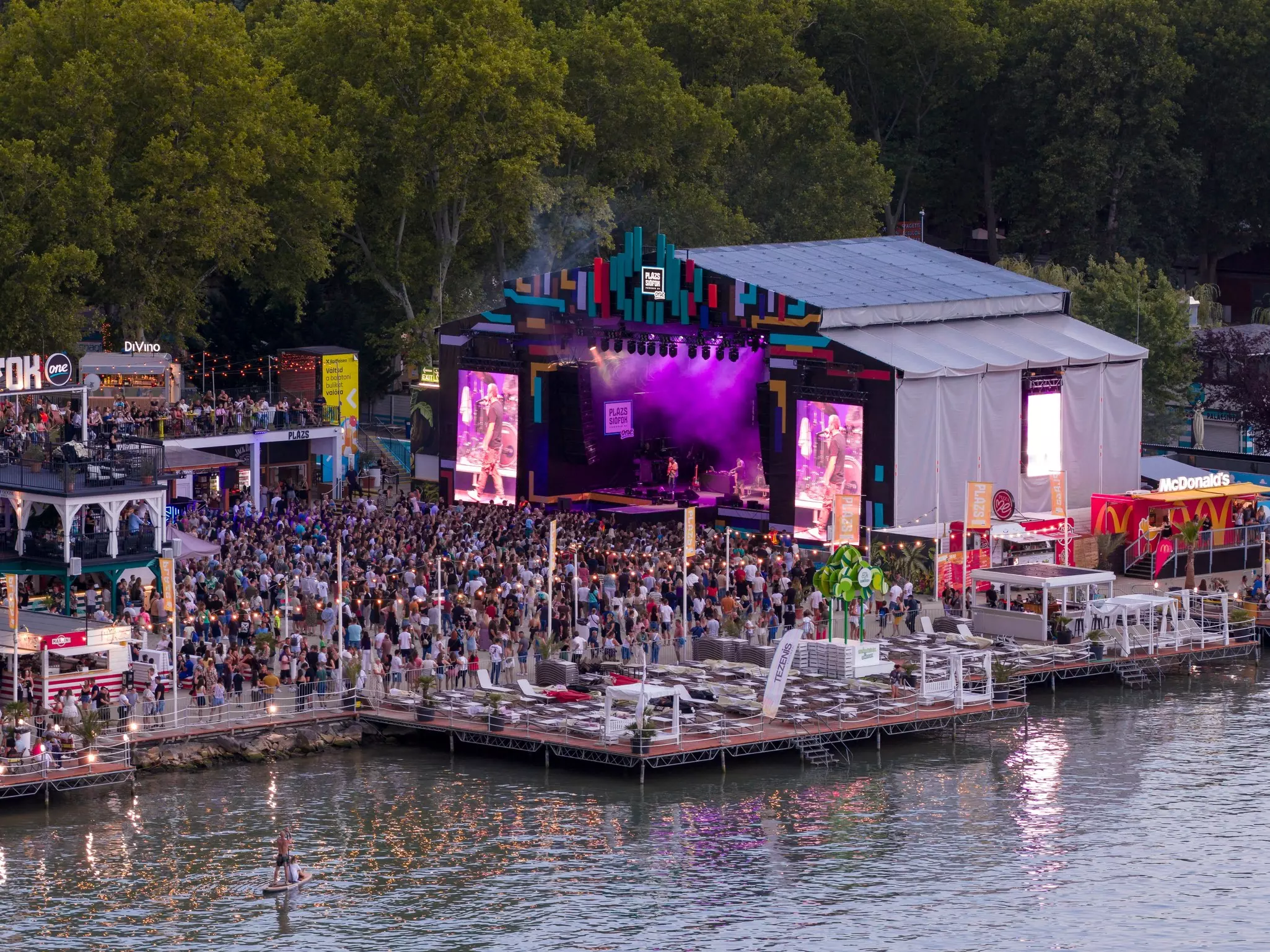 A wide shot of a crowded evening dance party on a platform by a lakeshore.