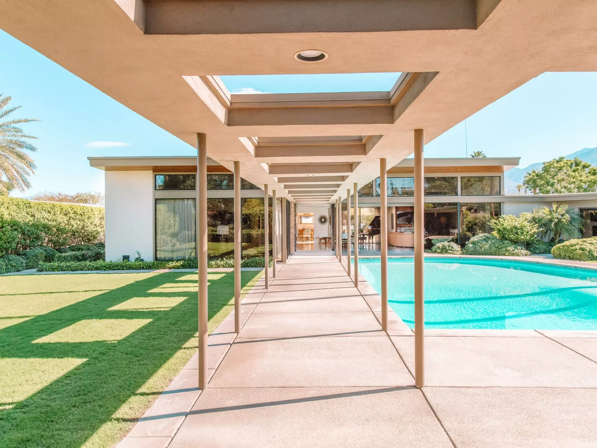 A covered walkway leads to a pool and a mid-century modern home.