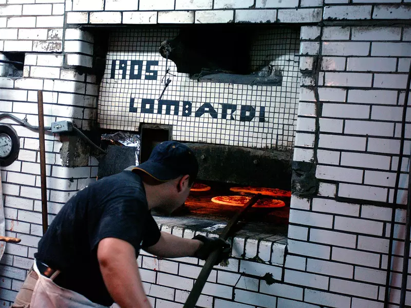A man pulls pizza from a pizza oven at Lombardi's Pizza in New York City's Little Italy