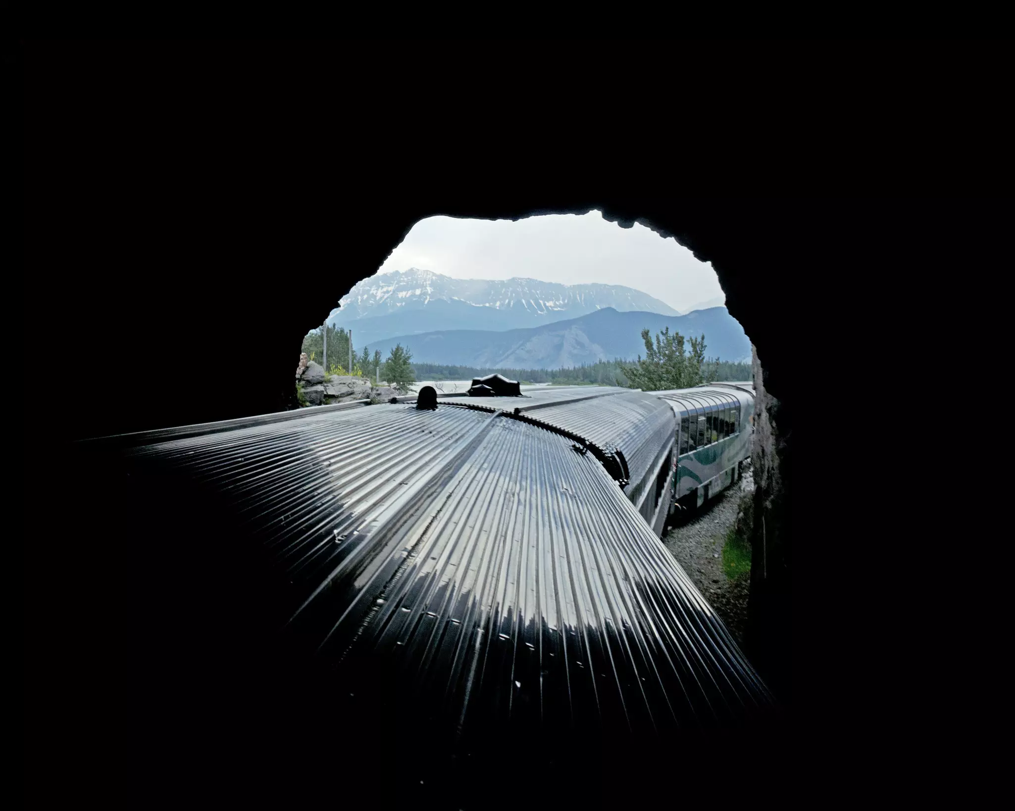 A train emerges from a dark tunnel into a mountainous landscape.
