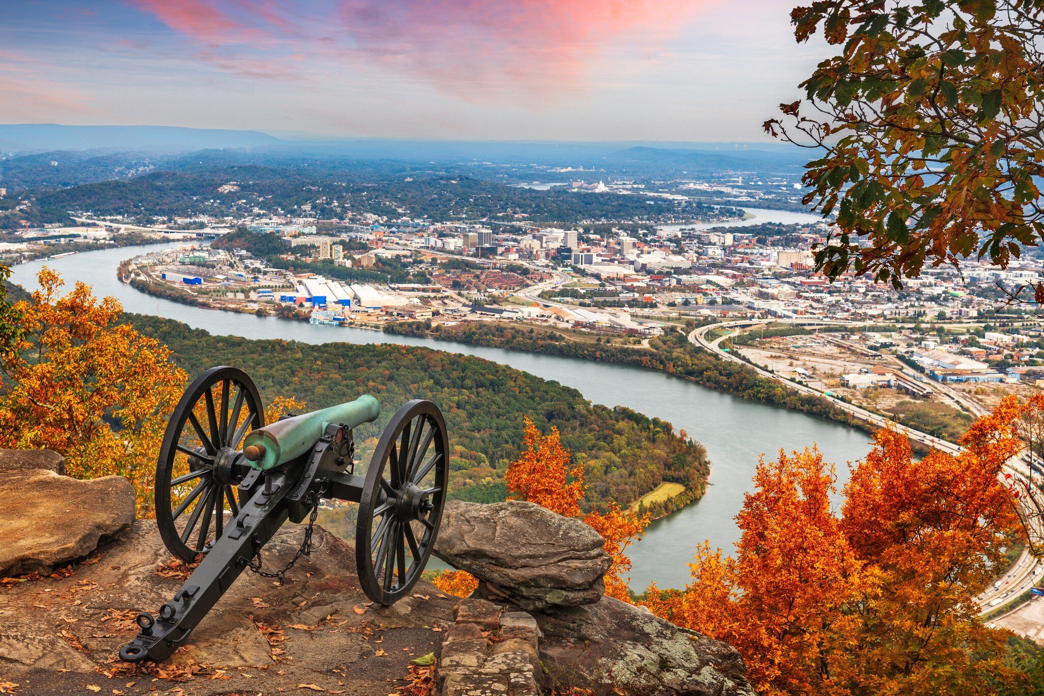 A river hairpin and city skyline seen from a clifftop with a cannon in the foreground