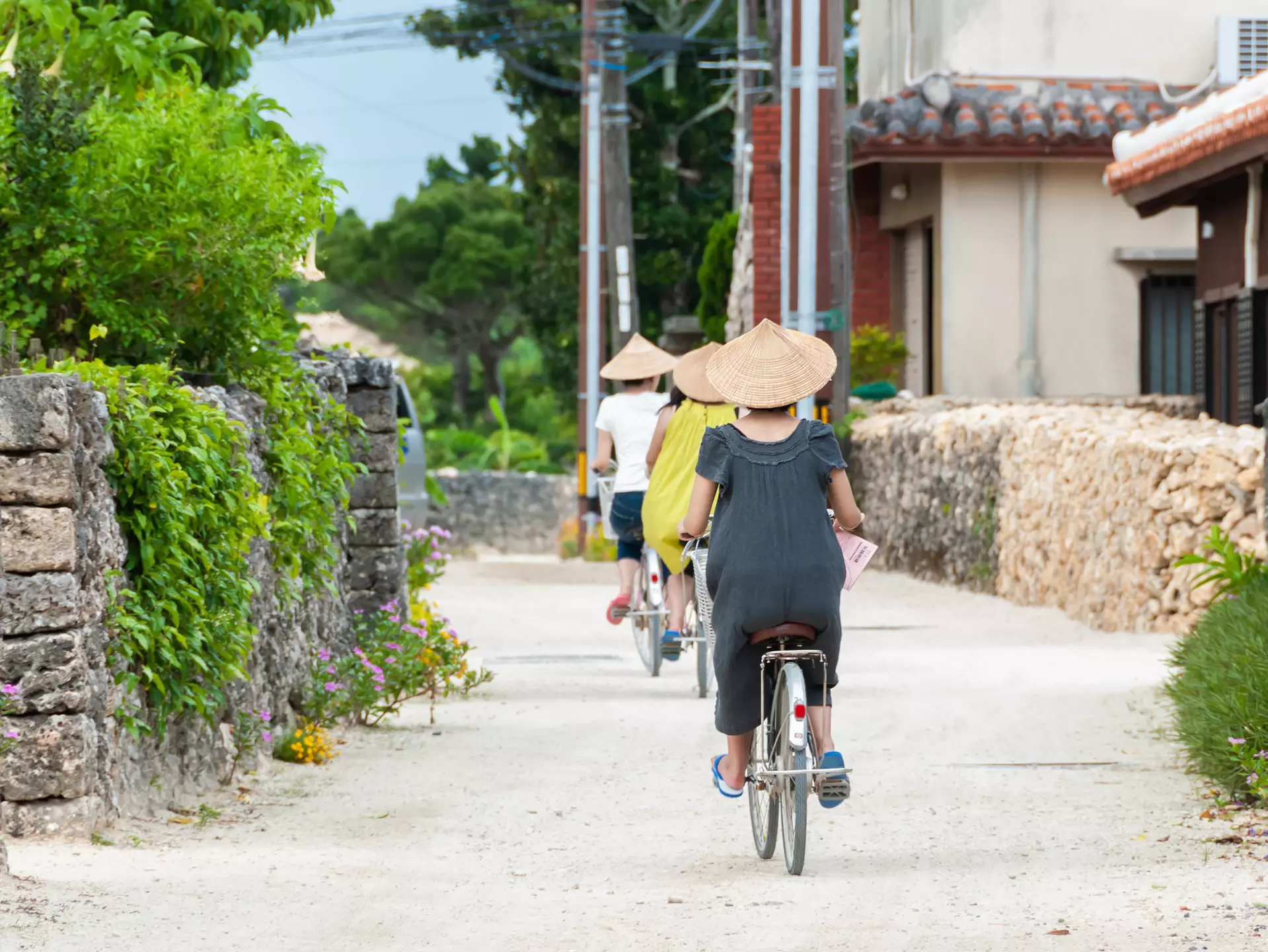 Three people wearing triangular hats while riding bikes along a dirt road