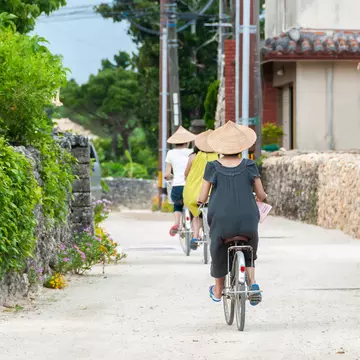 Three people wearing triangular hats while riding bikes along a dirt road