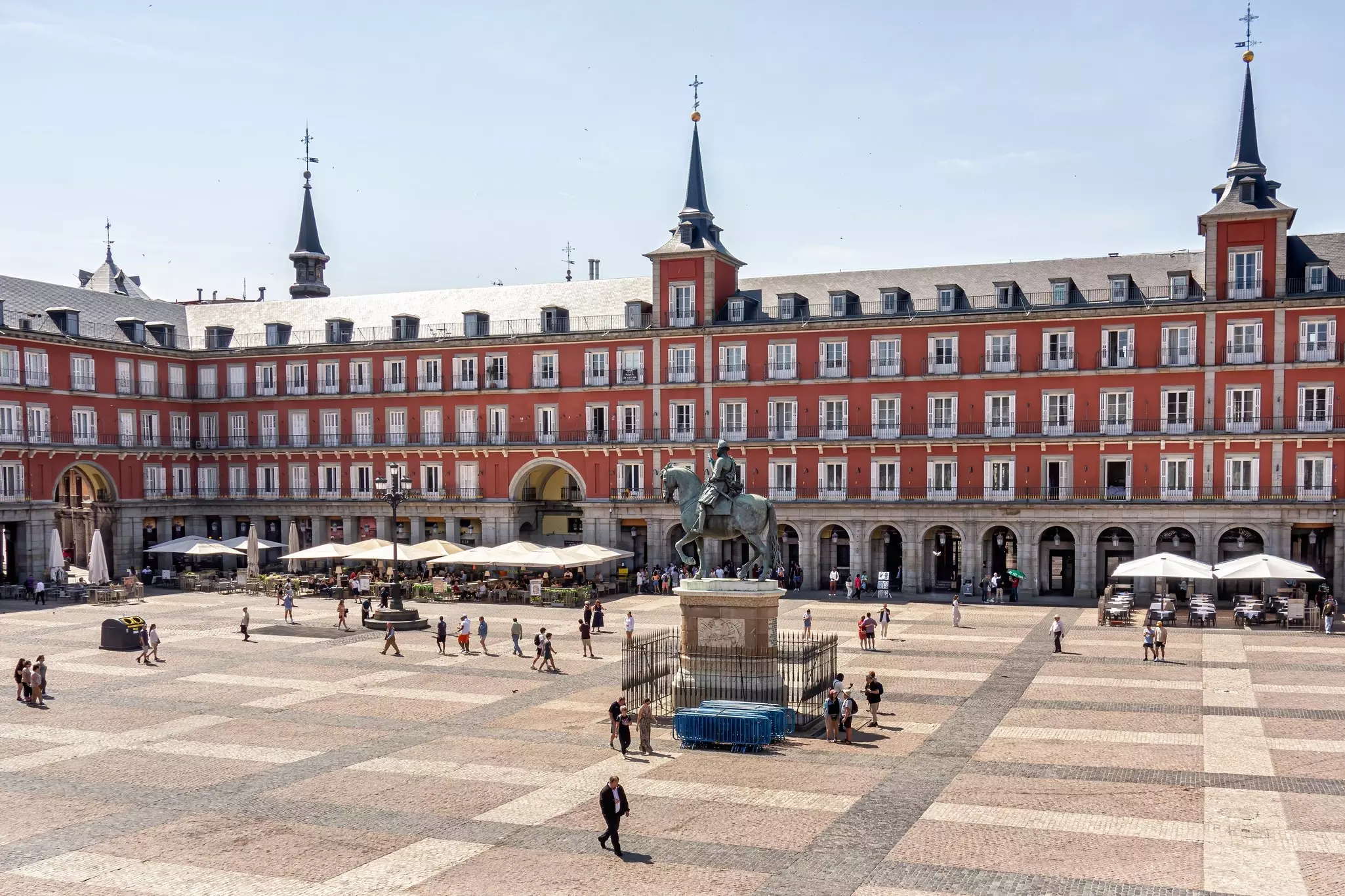 People pass through a large square surrounded by an ornate building with spires and balconied windows