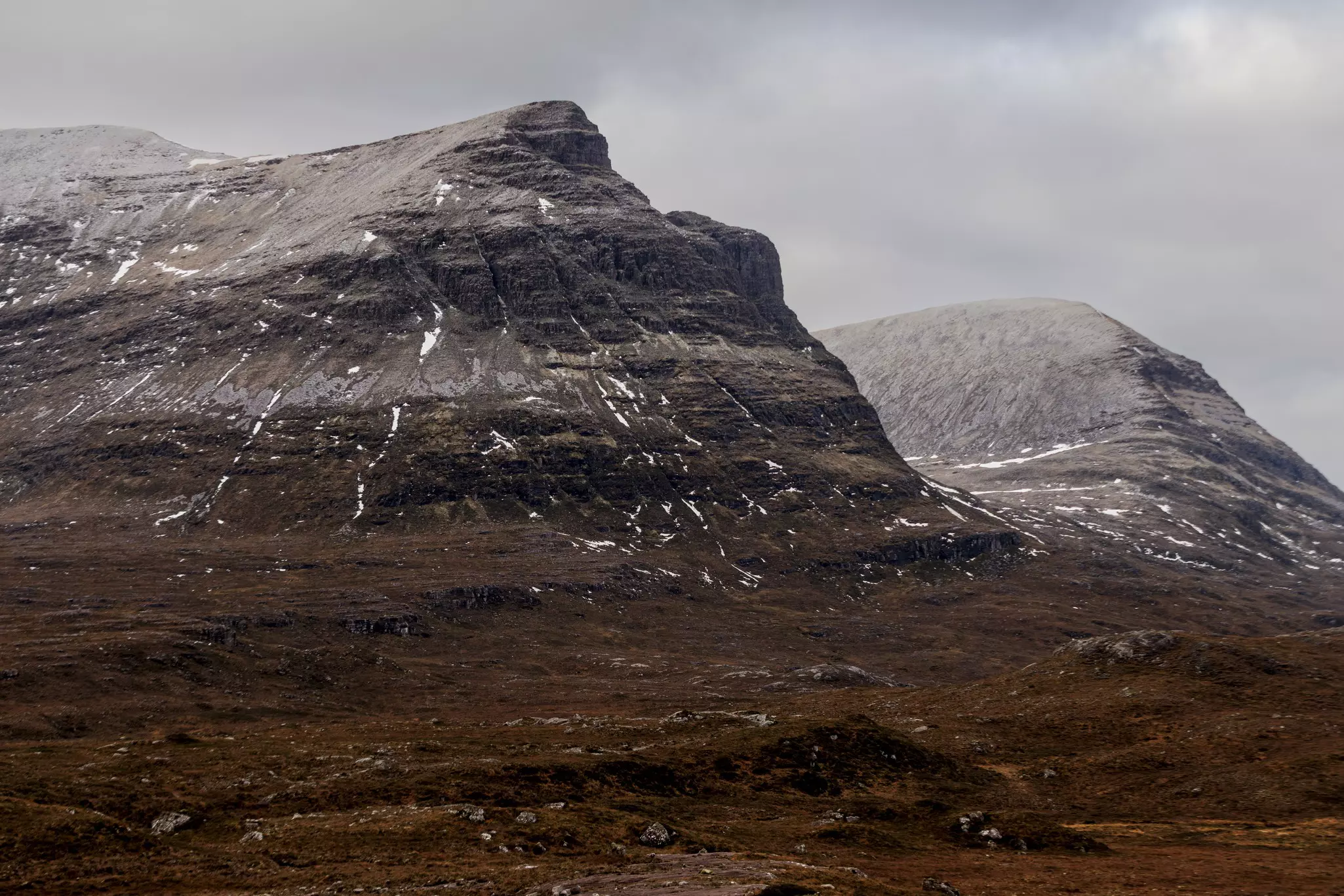 Mountains lightly dotted with snow around the Allt Chranaidh Waterfall on the NC500 driving route in Scotland.
