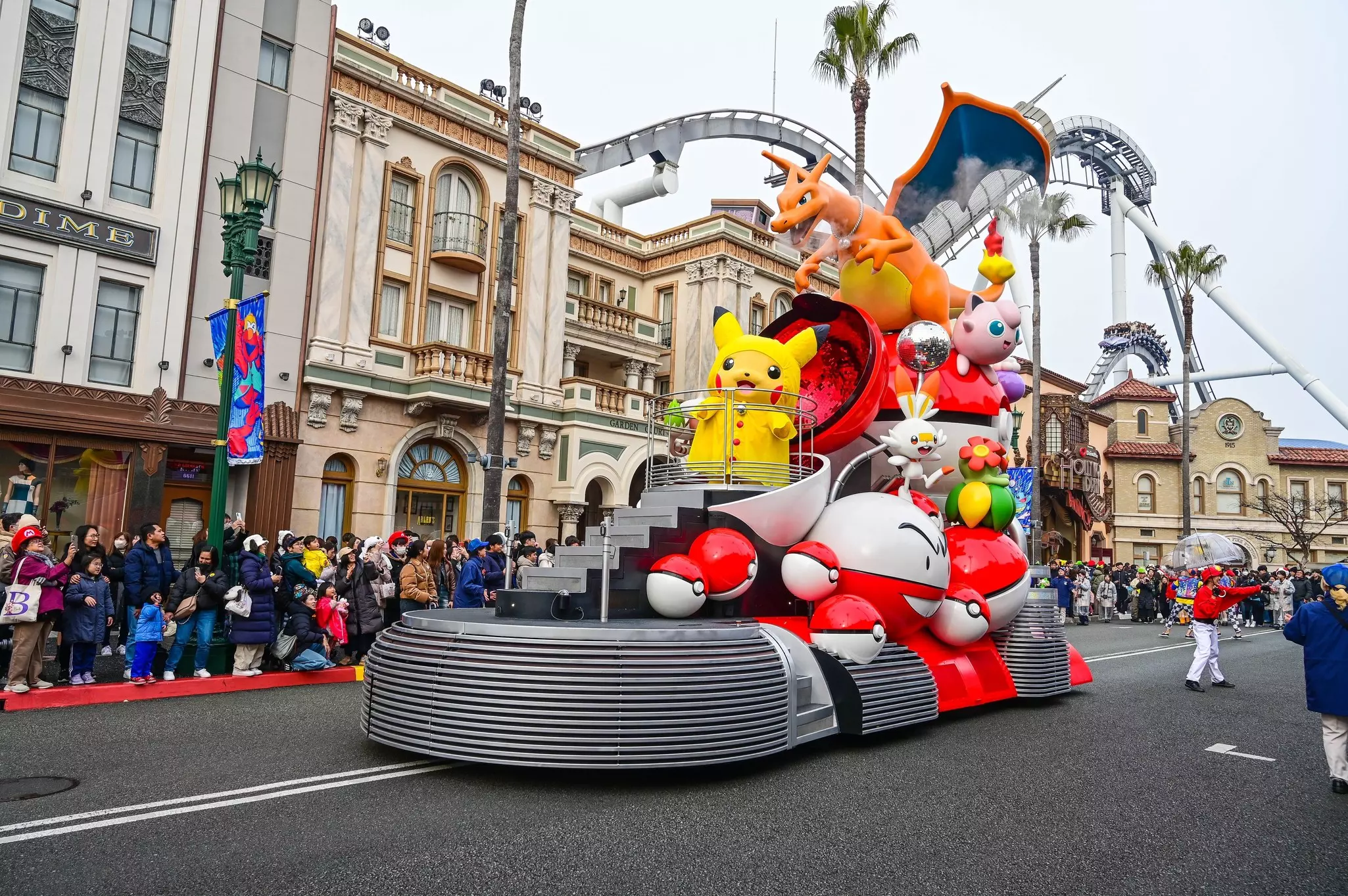 A float with inflated animated characters goes down a road at a theme park will spectators watch from the side.
