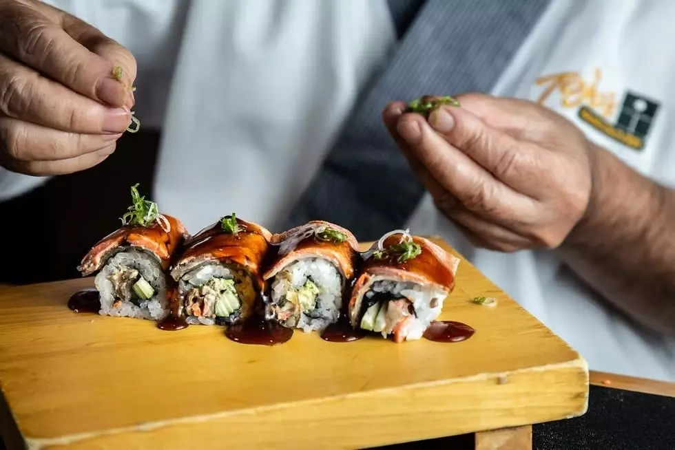 A chef prepares rolls of sushi on a wooden board.